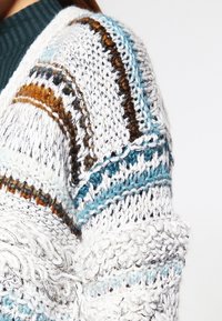 Chunky stickad kofta med vita, bruna och turkosa ränder. Texturerat garn med distinkta mönster och en lös passform.