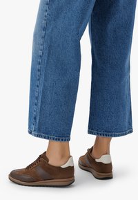 Pruunid tossud, mis sisaldavad segu nahast ja sametist, tekstureeritud disainiga, pehme tallaga ja kontrastsete heledate aktsentidega jalatsite kandmisel.