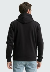 Schwarzer Kapuzenpullover mit Kordelzug, aus glattem Stoff, mit gerippten Bündchen und geradem Saum, getragen über hellblauen Jeans.