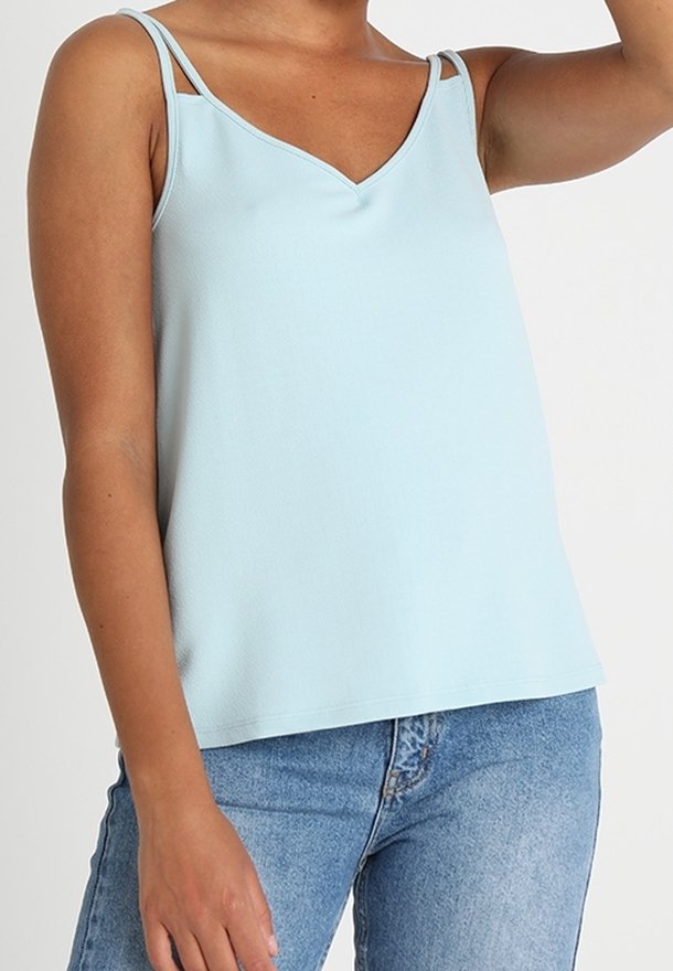 Ljusblå ärmlös topp med V-ringning och tunna axelband, som visar en texturerad tyg och avslappnad passform. Kombinerad med jeans i denim.