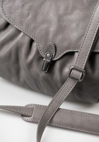 Borsa in pelle grigia con una texture morbida, dotata di chiusura a pattina, accessori metallici e una tracolla regolabile con cuciture in contrasto.