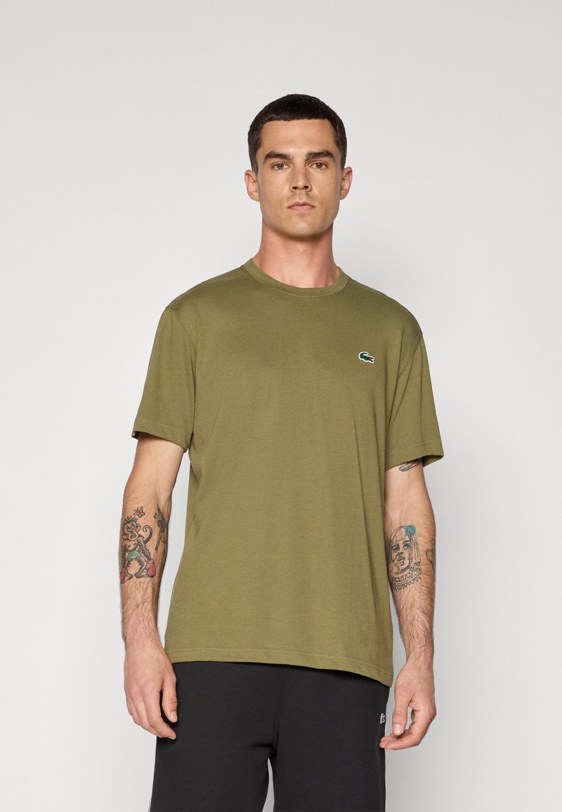 T-shirt de algodão verde oliva com decote redondo e mangas curtas, apresentando um pequeno logo da Lacoste no peito.