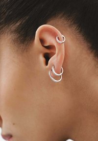 Pendientes de aro de plata en diferentes tamaños, con superficies lisas y texturizadas, llevados en la parte exterior de la oreja. Brillantes destellos sutiles de acentos incrustados.