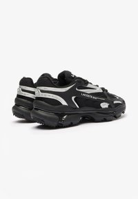Chaussures de sport noires avec une tige en mesh texturé, des accents argentés et une semelle noire épaisse et rembourrée. Présente un logo de marque prominent sur le côté.