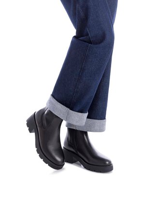 Botas de cuero negro hasta el tobillo con suela gruesa y paneles elásticos laterales, combinadas con jeans oscuros de mezclilla cuffed que muestran una textura de denim.