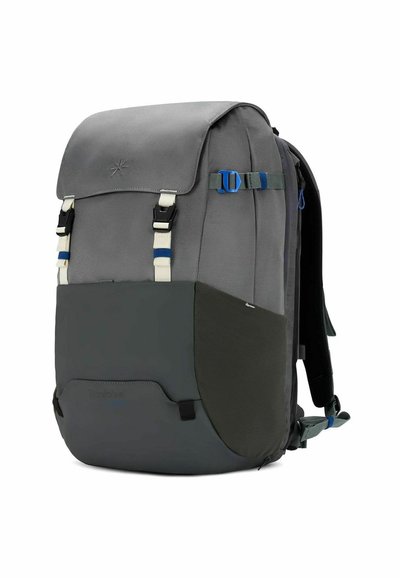 Mochila de tela gris con tapa superior, correas ajustables, detalles en azul y blanco, y un panel inferior texturizado. Presenta múltiples hebillas.