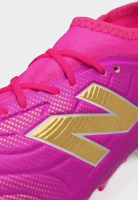 Gros plan sur une chaussure de sport rose avec des lacets roses et un grand logo doré sur le côté, orné de petits motifs de points dorés.