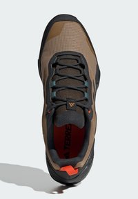 Brown synthetic outdoor shoe with mesh upper, black heel, textured sole, and orange accents. Features lace-up closure and padded collar.