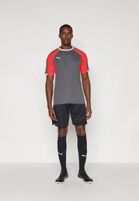 Hall ja punane lühikeste varrukatega spordipluus, millel on rinnal ja sokkidel logo, kombineeritud mustade lühikeste pükste ja sokkidega.