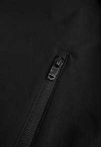 Zwarte stof met een close-up van een rits. De rits heeft een gladde trekker en een getextureerde tape ernaast.