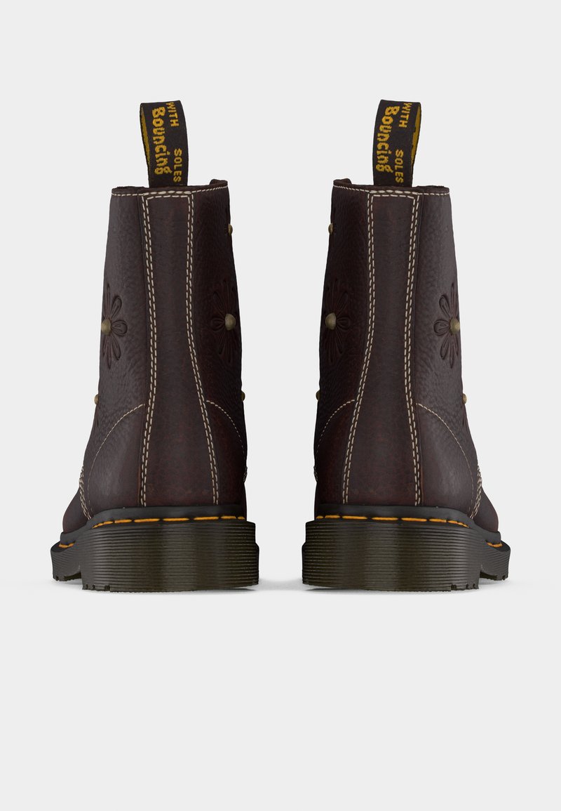 Dunkelbraune Lederstiefel mit floraler Prägung, gelben Zuglaschen mit der Aufschrift „With Bouncing Soles“ und dicken schwarzen Sohlen mit gelber Naht, von hinten gezeigt.