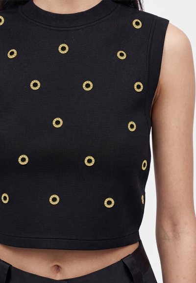 Μαύρο αμάνικο crop top με χρυσά κυκλικά τρουκς που είναι ομοιόμορφα τοποθετημένα μπροστά, φορεμένο από άτομο που δείχνει την κοιλιά και το δεξί μπράτσο.