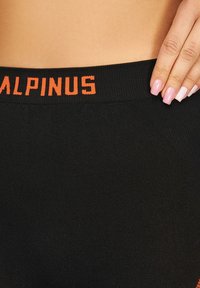 Czarne legginsy z elastycznym pasem w talii z nadrukiem "ALPINUS" w kolorze pomarańczowym. Gładka tekstura materiału, dopasowany krój, średni stan.