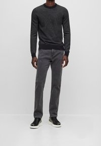 Suéter de punto gris oscuro con patrón texturizado, combinado con jeans grises y zapatillas negras con suelas blancas. Diseño simple y moderno.