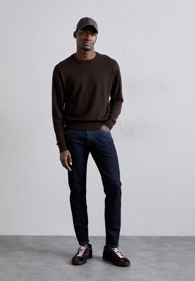 Suéter de punto marrón, jeans de denim oscuros, zapatillas burdeos y negras con cordones blancos, y una gorra a rayas. Diseño y textura simples y ajustados.