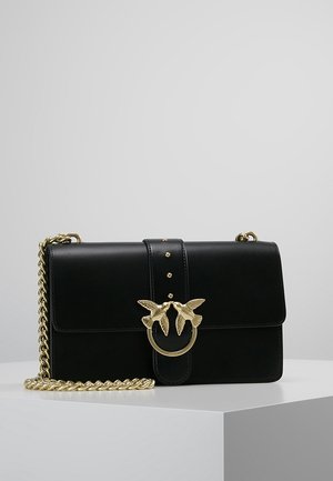 Bolso de cuero negro con herrajes dorados, que presenta un exclusivo motivo de pájaro y una correa de cadena. Textura suave con cierre de solapa y tachuelas decorativas.