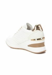 Zapatilla blanca con diseño acolchado, acentos dorados en el talón y la suela, y una gruesa plataforma blanca. Tejido texturizado y detalles metálicos.