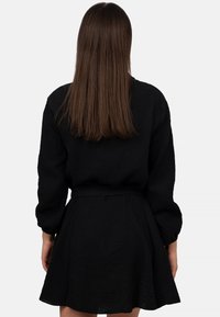 Abito nero con maniche lunghe a palloncino e gonna ampia, realizzato in un tessuto testurizzato. La vita è evidenziata da una cintura abbinata.