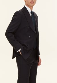 Granatowa marynarka w podwójny guziczek z narysowanymi klapami, z czterema guzikami, kieszeniami bocznymi i gładkim wykończeniem, noszona z kontrastowym krawatem.