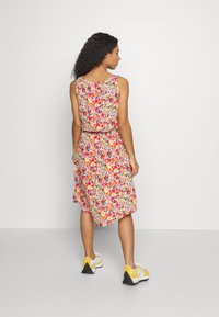 Vestido floral até aos tornozelos com um design sem mangas, cintura ajustada e padrões vibrantes de rosa, laranja e amarelo sobre um fundo claro.