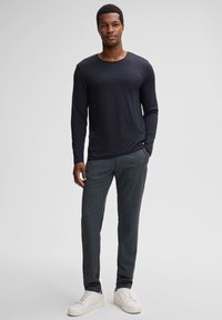 Marineblaues Langarmshirt mit Rundhalsausschnitt, kombiniert mit grauen gemusterten Hosen und weißen Sneakers. Schlichtes Design mit lockerer Passform.