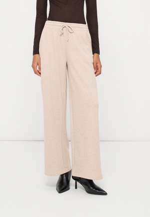 Personne portant un pantalon beige à jambes larges avec taille à cordon, un haut noir moulant à manches longues et des bottes noires à talons hauts pointues.