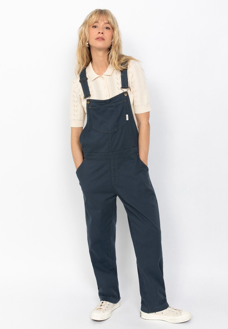 Marineblauwe overalls van duurzaam materiaal, met een ontspannen pasvorm, voorzakken, verstelbare banden en gouden hardware-accenten.