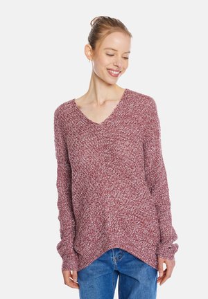 Maroon knitted sweater with a V-neck and dropped shoulders, featuring a textured pattern and side slits at the hem. Worn with blue jeans.