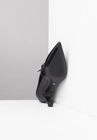 Zwarte leren hoge hakken met een spitse neus, gestructureerde buitenzool en een kleine blokhak. Bevat branding op de binnenzool.