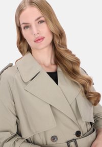 Bézs trench coat széles gallérral, dupla soros gombokkal és övvel a deréknál. Sima textúrájú, szabott kivitelű.