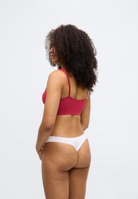 Hladký červený bralet s ramienkami na nastavenie, spárovaný s tenkým bielym tangom. Hladká tkanina, priliehavý strih. Jednoduchý a funkčný.