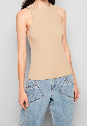 Débardeur beige à côtes avec un col montant et sans manches, associé à un jean large taille haute bleu clair avec des poches incurvées.