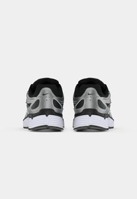 Un paio di scarpe da corsa Nike di colore argento, nero e bianco viste da dietro, con suole ammortizzate e loghi Swoosh Nike visibili.