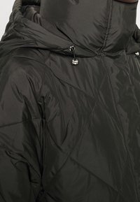 Giacca trapuntata nera in stile puffer con colletto alto, cappuccio con cordino e dettagli metallici, caratterizzata da una texture liscia e riflettente.