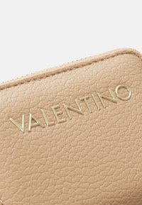 Carteira de couro bege com um acabamento texturizado, apresentando um logótipo dourado "VALENTINO". Fecho com zipper ao longo da borda.