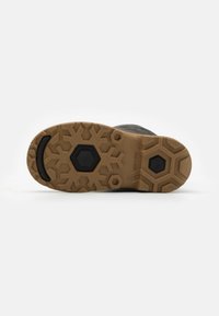 Semelle en caoutchouc avec un design robuste comprenant des motifs hexagonaux et en flocon de neige, principalement de couleur marron avec des accents noirs.