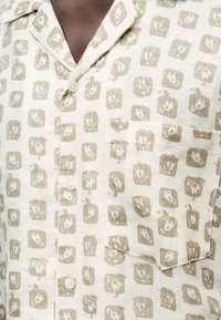 Μπεζ πουκάμισο με κουμπιά, γιακά και τσέπη στο στήθος, με σχέδιο από ανοιχτό καφέ τετράγωνες μπλοκ με λουλουδένια μοτίβα.