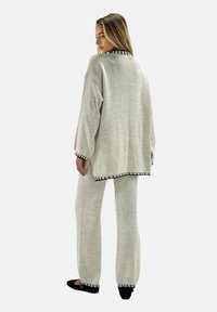 Conjunto de punto beige con suéter de corte holgado y pantalones, con ribetes negros en los puños y el dobladillo. Textura suave y silueta relajada.