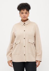 Beige button-up shirt made of soft fabric, featuring a collar, two front pockets, and gold-tone buttons. Long sleeves with cuffs.