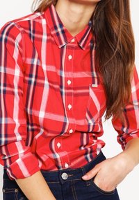 Chemise à carreaux rouge et bleu, avec un col, des manches longues et une poche frontale. Fabriquée en tissu léger avec une coupe décontractée.