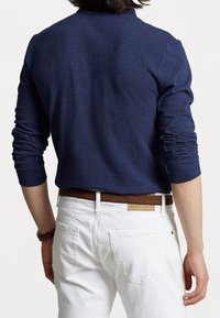 Námořnický polo triko s dlouhým rukávem z texturované látky, s ohrnutými rukávy, nošené s bílými džínami a hnědým koženým pásem s kovovým akcentem.