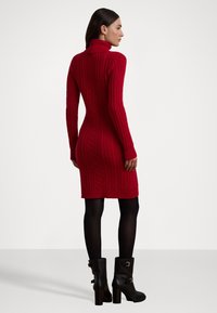 Rochie tricotată roșie cu un guler înalt, siluetă ajustată, tiv cu nervuri și mâneci lungi, asortată cu cizme negre cu toc.