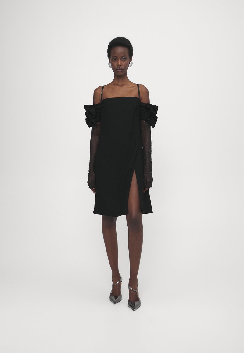 Czarna sukienka z falbanami na ramiączkach, przezroczystymi długimi rękawami oraz rozcięciem z przodu. Gładki materiał z dopasowanym krojem, sięgająca kolan.