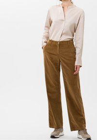 Bruna kordfloddsbyxor med vida ben, framfickor, knappstängning och en slät beige skjorta med krage. Texturerat tyg med vertikala ribbor.