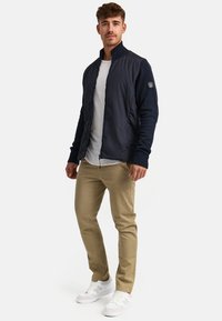 Navy bomber jacket with knit sleeves, zip front, and ribbed collar. Paired with beige pants and white sneakers.