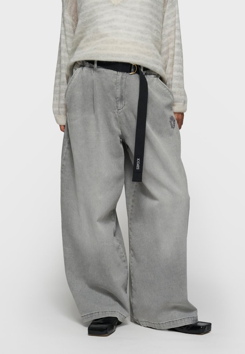 Pantalones de mezclilla gris de pierna ancha con un acabado texturizado, que cuentan con un cinturón negro y un detalle bordado en el bolsillo.