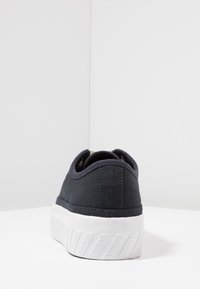 Baskets noires en toile avec une semelle en caoutchouc blanche, présentant un design bas et des accents texturés. Détails de couture simples le long du talon.