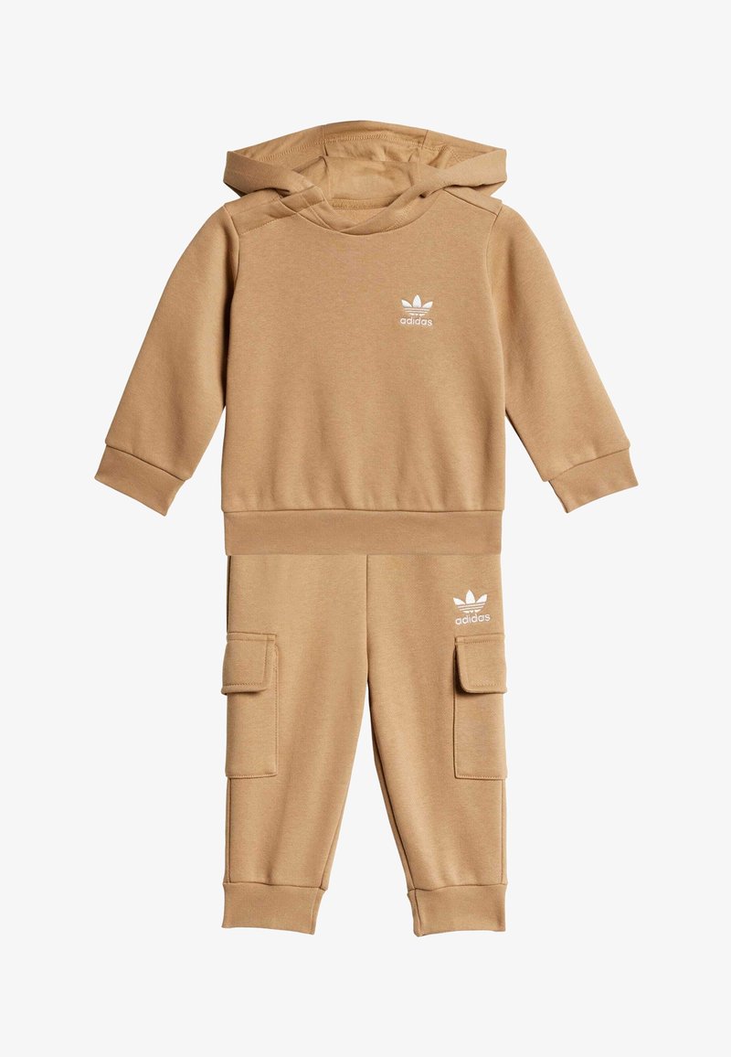 Beige hoodie en broekset van zachte stof. De hoodie heeft een klein wit logo, terwijl de broek cargozakken en aansluitende boorden heeft.