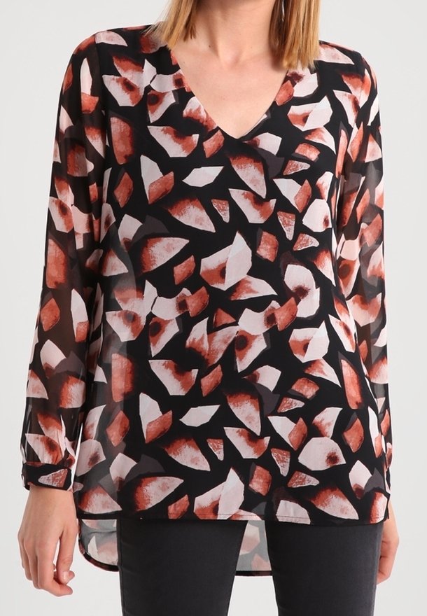 Femme portant un chemisier noir à manches longues avec un motif abstrait de feuilles rouges et blanches et un décolleté en V, assorti à un pantalon noir.