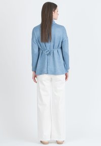 Sininen, pitkähihainen paita, jossa on sidottu vyötäröyksityiskohta, valmistettu pehmeästä kankaasta. Yhdistetty korkeavyötäröisiin valkoisiin leveälahkeisiin housuihin.